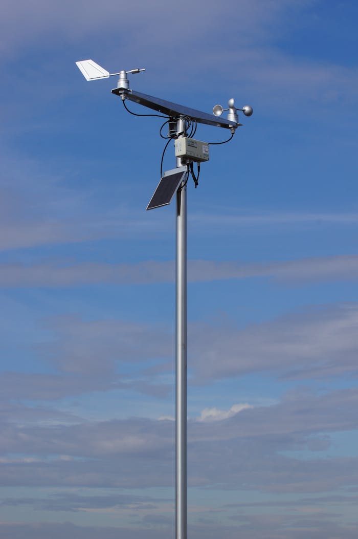 Anemometer and weather vane atop a tall pole under a clear blue sky.