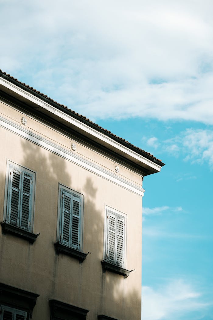 A vintage Croatian building facade with shutters casting shadows under a clear blue sky.